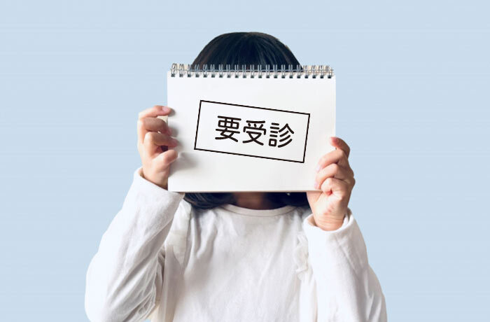 要受診と書かれたノートで顔を隠す子供