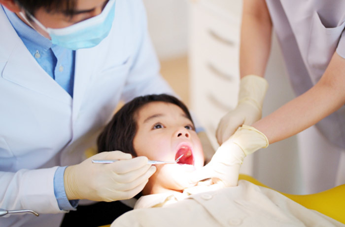 歯科医院の明るいライトの下で口腔内をチェックしてもらっている小学生