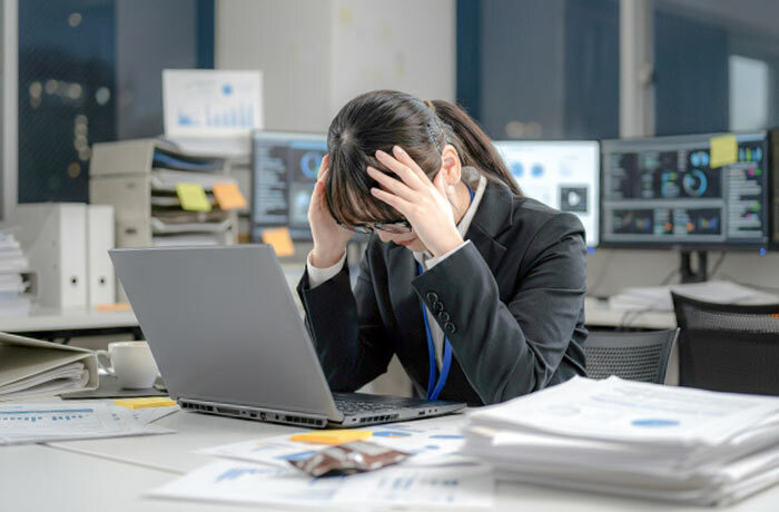 オフィスの雑多な机に置かれたパソコンの前で頭を抱えてうつむく女性社員