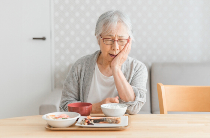 食事を前にして、頬を抑えて痛みを堪える高齢の女性