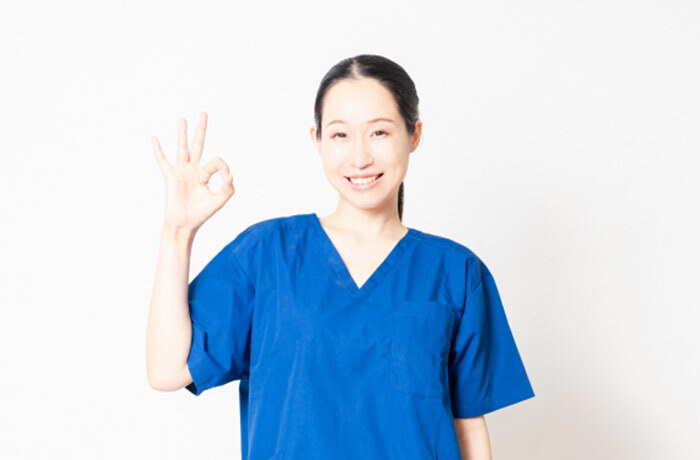 右手でOKサインを出し、笑顔でこちらを見る女性歯科医師