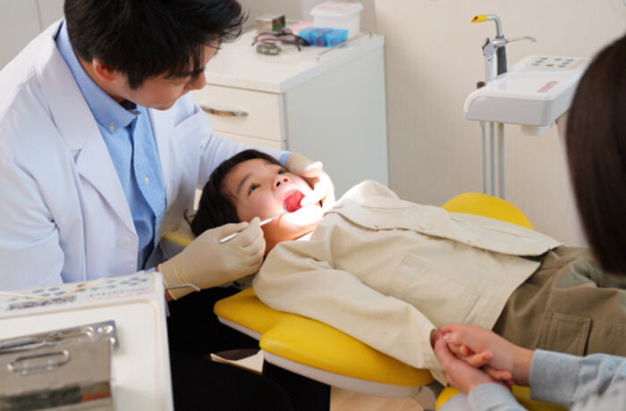 歯科医院のユニットで、歯科医師に口腔内をチェックしてもらっている子供の画像